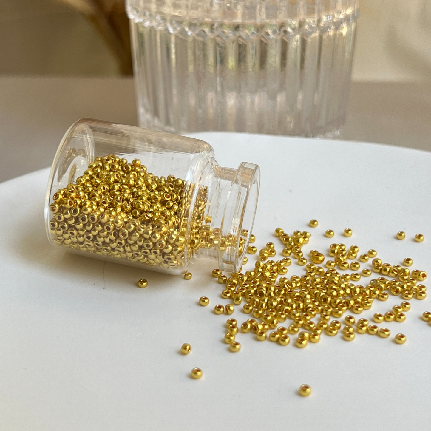 Tiny golden seed beads stored in a small glass vial, perfect for jewelry crafting