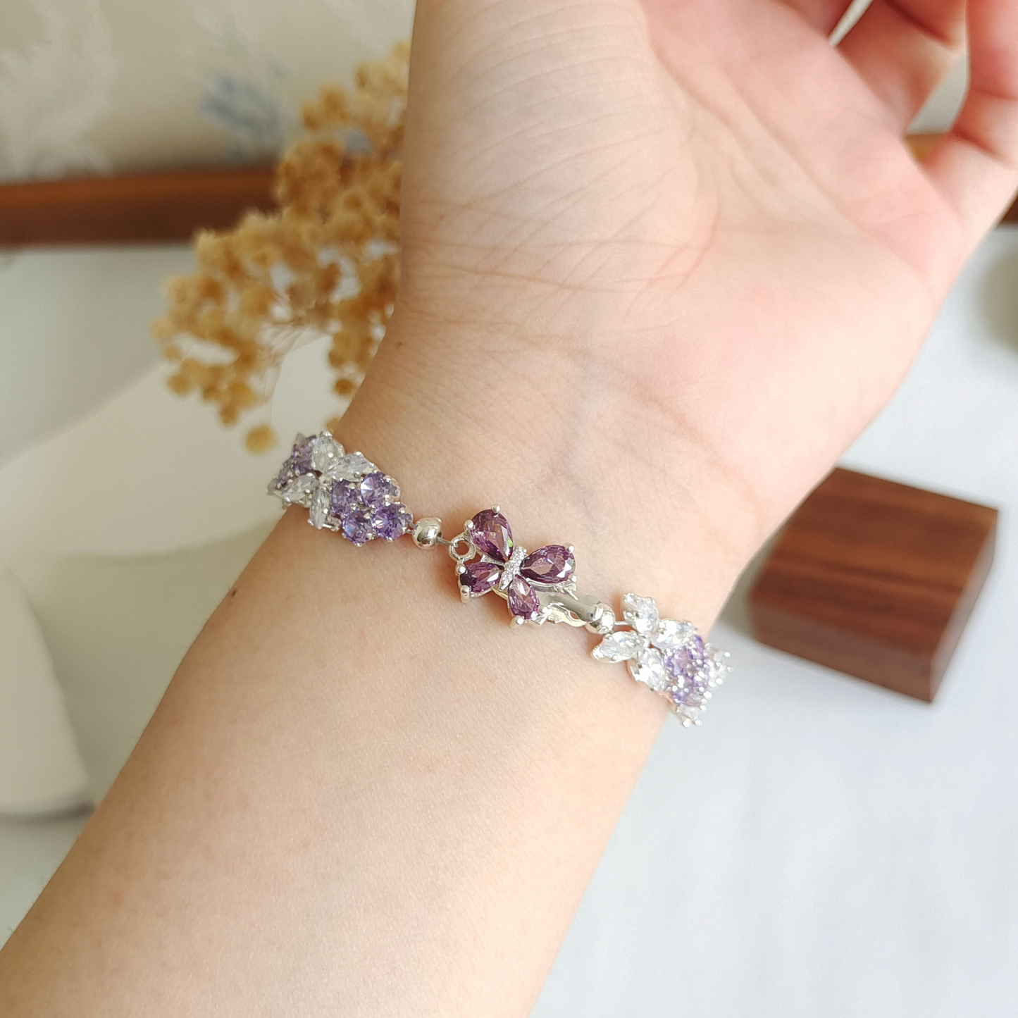On-wrist view of a silver bracelet with violet gems and crystal butterflies.