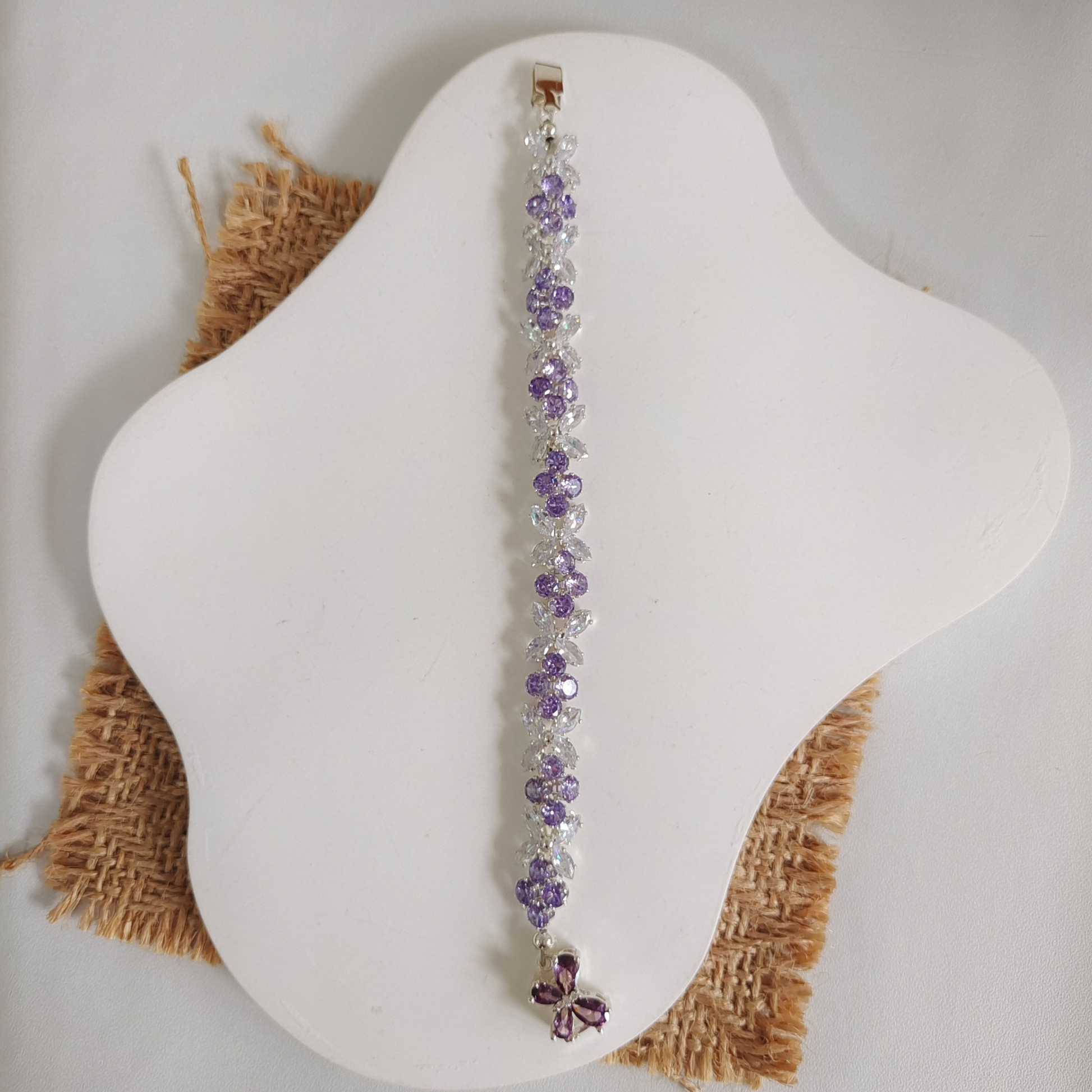 Flat lay of a purple and clear zircon butterfly bracelet on a white cushion.